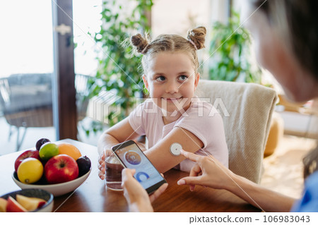 Girl with diabetes checking blood glucose level at home using continuous glucose monitor. 106983043