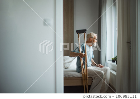 Senior man with crutches spending time alone in his apartment. 106983111