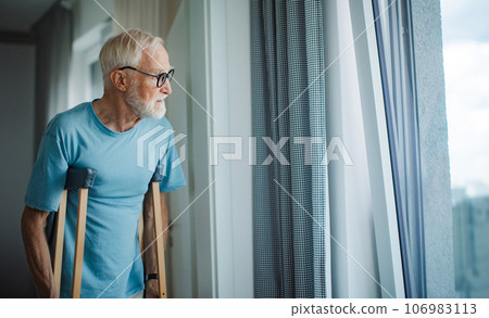 Senior man with crutches spending time alone in his apartment. 106983113