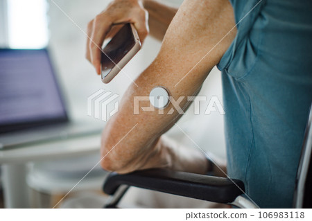 Diabetic senior man checking blood glucose level at home using continuous glucose monitor. 106983118