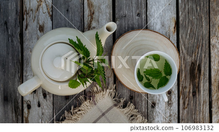 Top view of a teapot and tea cup with homemade nettle tea on a wooden table. 106983132
