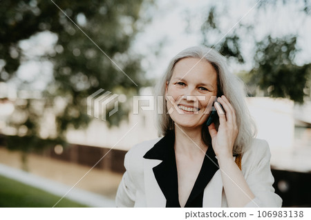 Portrait of beautiful female manager in middle age with gray hair walking through the city. 106983138
