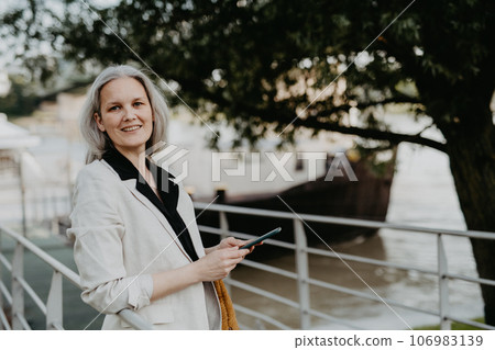 Portrait of beautiful female manager in middle age with gray hair walking through the city. 106983139