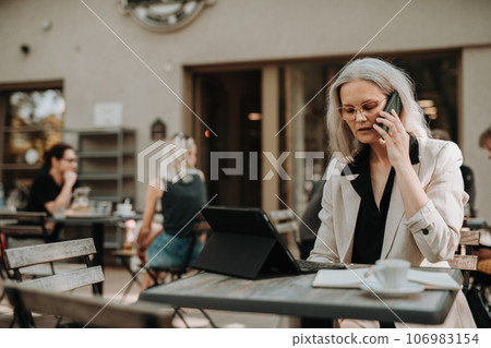 Portrait of beautiful female manager in middle age with gray hair making a phone call outdoors. Portrait of beautiful female manager in middle age with gray hair making a phone call outdoors. 106983154