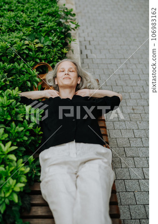 Shot from above of a beautiful woman with gray hair lying on the bench in city park. Shot from above of a beautiful woman with gray hair lying on the bench in city park. 106983162