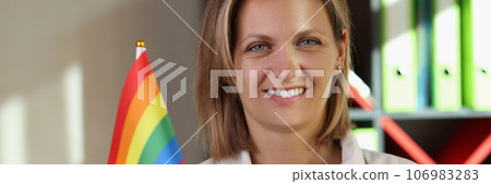 Smiling female doctor holds rainbow lgbt flag in her hand in medical clinic. Smiling female doctor holds rainbow lgbt flag in her hand in medical clinic. 106983283