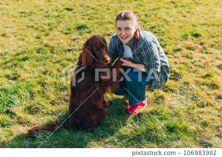 Human and a dog. Woman and her friend dog on the straw field background. Beautiful Irish Setter dog is sitting in grass. Domestic animals concept 106983982
