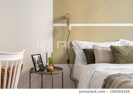 Fragment of a hotel room in olive-beige tones with a double bed, a bedside table and decorative accessories. The concept of a cozy hotel room for long stays and business trips. Copyspace 106984268