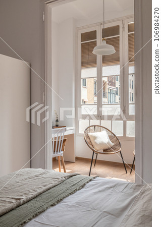 View from the bed covered with light-coloured bedclothes to the straw chair standing near the window overlooking the courtyard of the hotel. The concept of cozy apartments in the hotel View from the bed covered with light-coloured bedclothes to the straw chair standing near the window overlooking the courtyard of the hotel. The concept of cozy apartments in the hotel 106984270