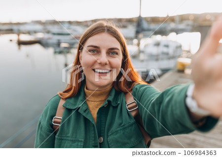 Happy 30s Women taking selfie. Young beautiful girl say Hi Tourist walking along the waterfront, seaside. Vacation concept by exploring interesting places to travel 106984363