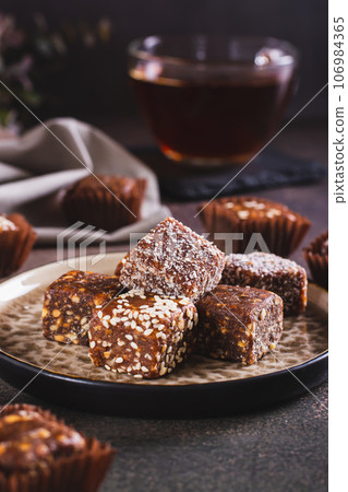 Healthy candies made from figs, dates, nuts, coconut and sesame seeds on a plate vertical view 106984365