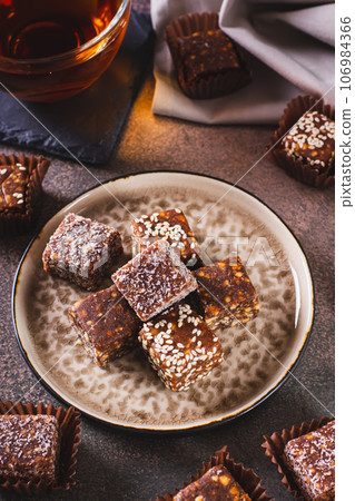Sugar free candies made from fruit paste, nuts and sesame seeds on a plate vertical view Sugar free candies made from fruit paste, nuts and sesame seeds on a plate vertical view 106984366