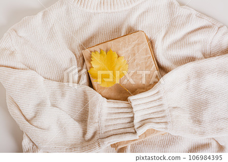 Cozy autumn old book and autumn leaf on a knitted sweater top view Cozy autumn old book and autumn leaf on a knitted sweater top view 106984395