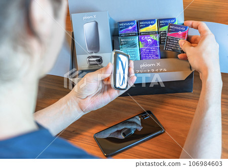 A man picks up a pack of Mobius brand electronic cigarettes in a Ploom X free trial box. 106984603
