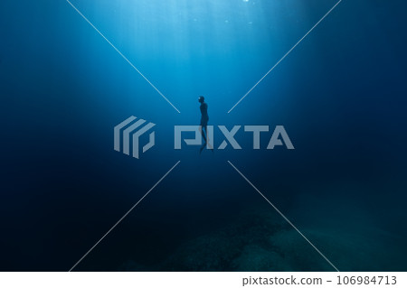 Freediver Swimming in Deep Sea With Sunrays. Young Man DIver Eploring Sea Life. Freediver Swimming in Deep Sea With Sunrays. Young Man DIver Eploring Sea Life. 106984713