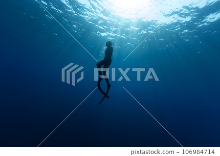 Freediver Swimming in Deep Sea With Sunrays. Young Man DIver Eploring Sea Life. 106984714