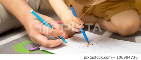 Little toddler boy of two or three years old with dad draws with markers in the album in the children's room at home sitting on the floor. Spending time with children. Selective focus 106984736