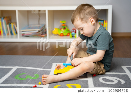 A little toddler boy is playing with a toy helicopter, assembling and disassembling it. Educational toys for kids. Children's room in home. Indoors 106984738