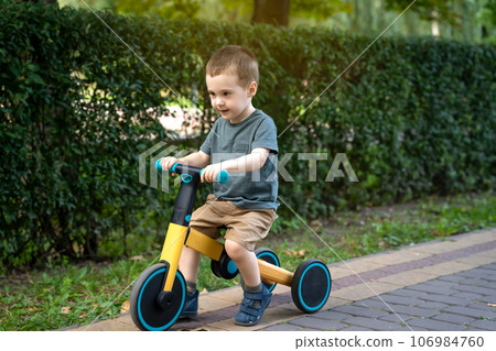 A cute toddler boy of two or three years old rides a bicycle or balance bike in a city park on a sunny summer day. Toddlerhood and childhood concept. Selective focus 106984760