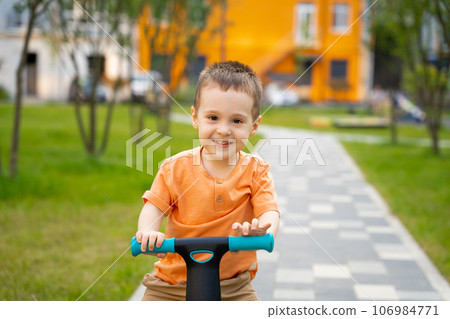 A cute happy toddler boy of two or three years old rides a bicycle or balance bike in a residential complex on a sunny summer day. Active kid playing outside. Close up A cute happy toddler boy of two or three years old rides a bicycle or balance bike in a residential complex on a sunny summer day. Active kid playing outside. Close up 106984771