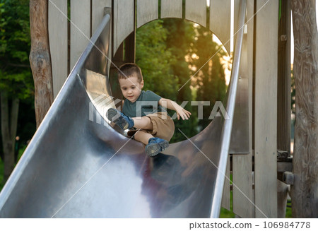 A cute toddler boy of two or three years going down the slide in the playground on a summer day. Active kid playing outside. Selective focus 106984778