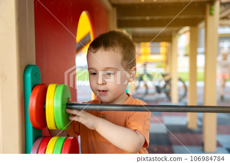 Cute toddler boy two or three years old is playing on the playground with wooden colorful rings on a sunny summer day. Children's games. Close-up. Selective focus Cute toddler boy two or three years old is playing on the playground with wooden colorful rings on a sunny summer day. Children's games. Close-up. Selective focus 106984784