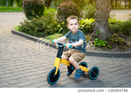 A cute toddler boy of two or three years old rides a bicycle or balance bike in a city park on a sunny summer day. Toddlerhood and childhood concept. Selective focus 106984786