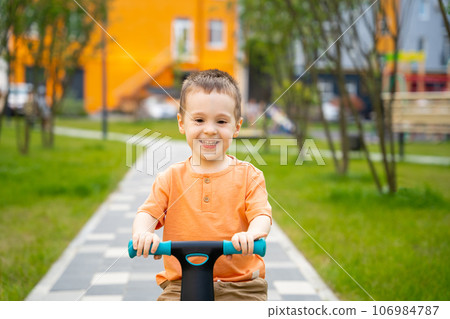 A cute happy toddler boy of two or three years old rides a bicycle or balance bike in a residential complex on a sunny summer day. Active kid playing outside. Close up A cute happy toddler boy of two or three years old rides a bicycle or balance bike in a residential complex on a sunny summer day. Active kid playing outside. Close up 106984787
