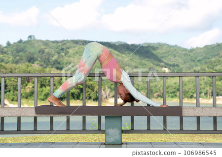 yogi girl in vibrant yoga sportswear performs stretch in open gazebo yogi girl in vibrant yoga sportswear performs stretch in open gazebo 106986545