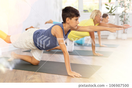Mother, grandmother and adolescence son do bird dog Dandayamana Bharmanasana Balancing Table pose 106987500