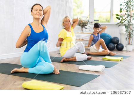 Middle-aged woman practicing cow face pose of yoga in light fitness room Middle-aged woman practicing cow face pose of yoga in light fitness room 106987507