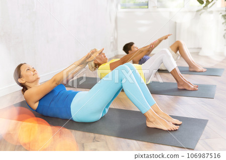 Group of people lying on floor doing yoga exercise boat pose. Group of people lying on floor doing yoga exercise boat pose. 106987516