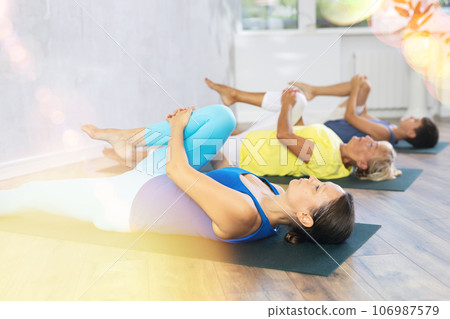 Mom, grandmother and teen grandson do preparatory stretching, lying on back and benting leg at knee Mom, grandmother and teen grandson do preparatory stretching, lying on back and benting leg at knee 106987579