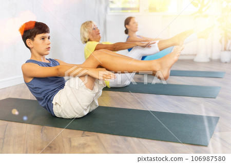 Preteen boy practicing boat pose of yoga in light fitness room Preteen boy practicing boat pose of yoga in light fitness room 106987580