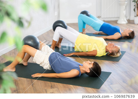 Mom, grandmother and teen grandson performing exercises with softball lying on floor Mom, grandmother and teen grandson performing exercises with softball lying on floor 106987639