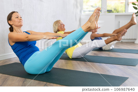Middle-aged woman practicing boat pose of yoga in light fitness room 106987640