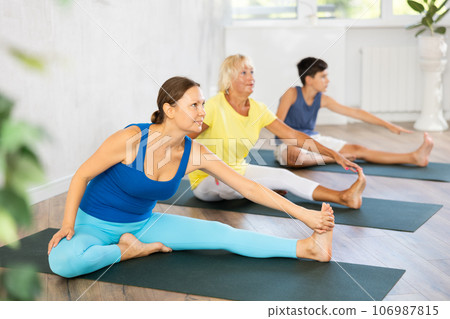 Middle-aged woman practicing head to knee pose of yoga in light fitness room Middle-aged woman practicing head to knee pose of yoga in light fitness room 106987815
