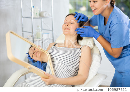 Cosmetologist examine patients contour face after lifting oval of face and palpate cheekbones Cosmetologist examine patients contour face after lifting oval of face and palpate cheekbones 106987831
