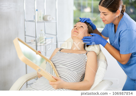 Cosmetologist examine patients contour face after lifting oval of face and palpate cheekbones Cosmetologist examine patients contour face after lifting oval of face and palpate cheekbones 106987854