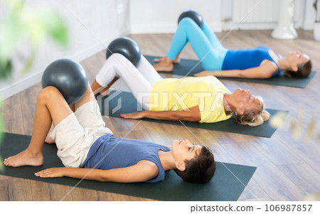 Mom, grandmother and teen grandson performing exercises with softball lying on floor Mom, grandmother and teen grandson performing exercises with softball lying on floor 106987857