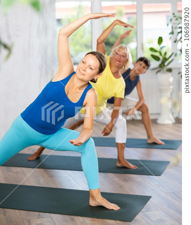 Middle-aged woman practicing side angle pose of yoga in light fitness room 106987920