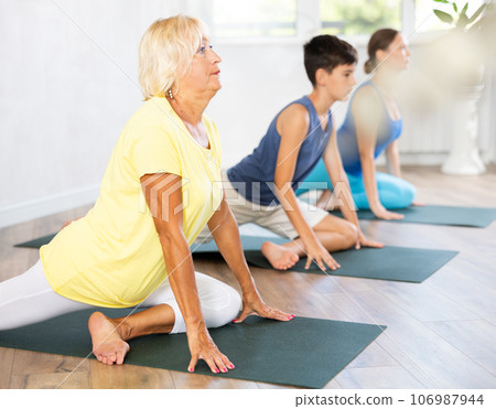 Mother, grandmother and teen son do exercise dove pose, Eka Pada Rajakapotasana. Mother, grandmother and teen son do exercise dove pose, Eka Pada Rajakapotasana. 106987944