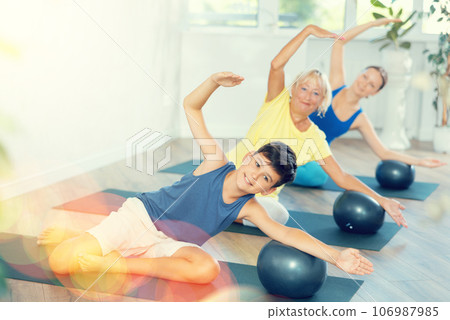 Family grandmother, mother and grandson perform fitness exercise sitting on floor with softball Family grandmother, mother and grandson perform fitness exercise sitting on floor with softball 106987985