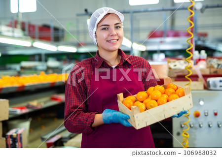 Smiling young female fruit warehouse worker with box of mandarins Smiling young female fruit warehouse worker with box of mandarins 106988032