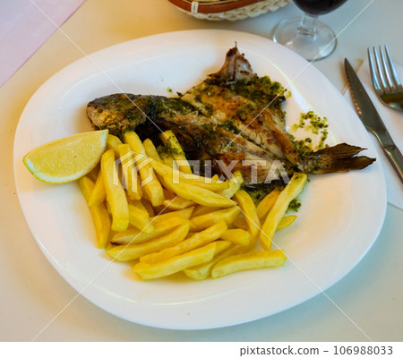 Baked in oven dorado fish with lemon and french fries served Baked in oven dorado fish with lemon and french fries served 106988033