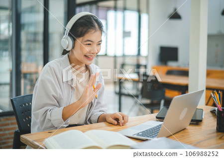 Teenage Asian students wearing a headphone are communicating through video conferencing for online learning. In a video conference call via apps. Teenage Asian students wearing a headphone are communicating through video conferencing for online learning. In a video conference call via apps. 106988252
