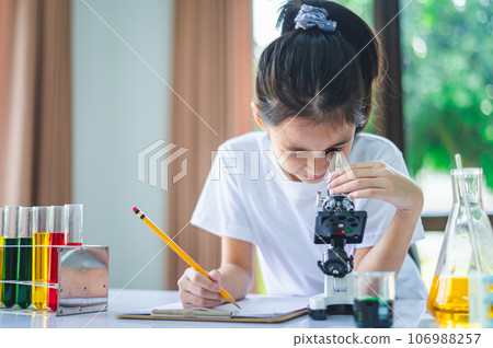 little scientist looking through a microscope and test tubes filled with chemicals for learning about science and experiments. little scientist looking through a microscope and test tubes filled with chemicals for learning about science and experiments. 106988257