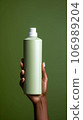 Female hand holding a bottle of body lotion on a green background 106989204
