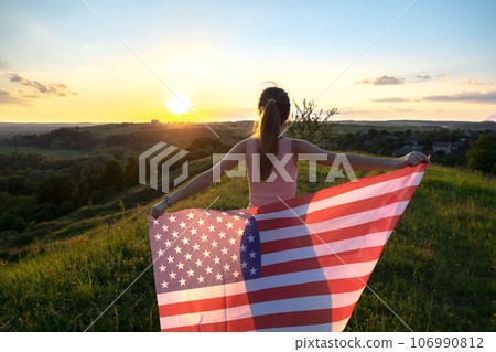 Young woman posing with USA national flag outdoors at sunset. Positive girl celebrating United States independence day. 106990812
