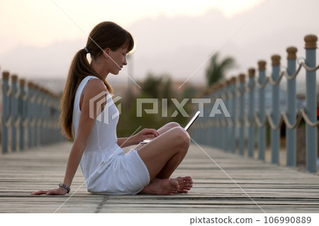 Young female office worker working on laptop computer outdoors on warm summer evening. Remote work and study concept. Young female office worker working on laptop computer outdoors on warm summer evening. Remote work and study concept. 106990889
